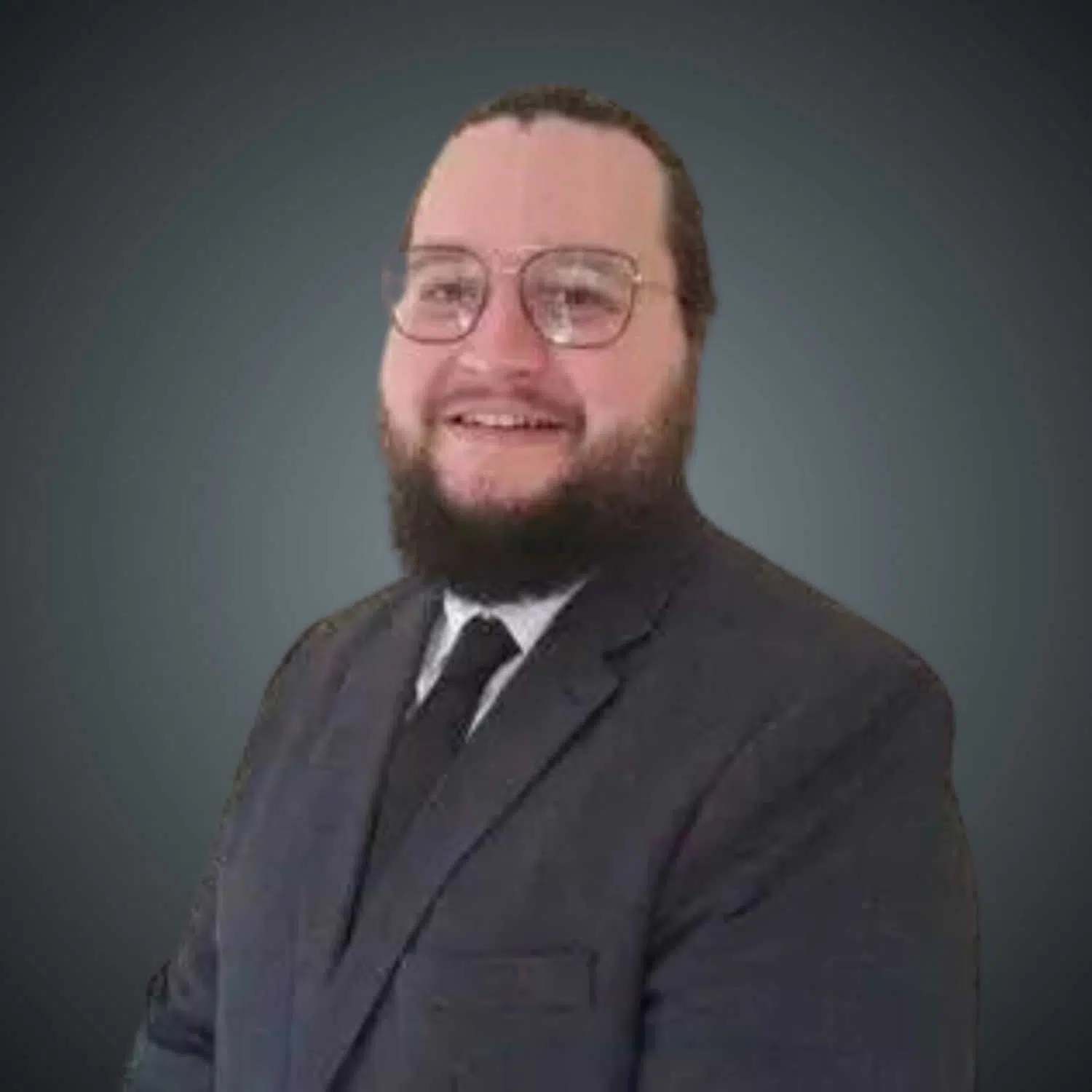 Smiling man with a beard and glasses wearing a dark suit, white shirt, and black tie against a gray background