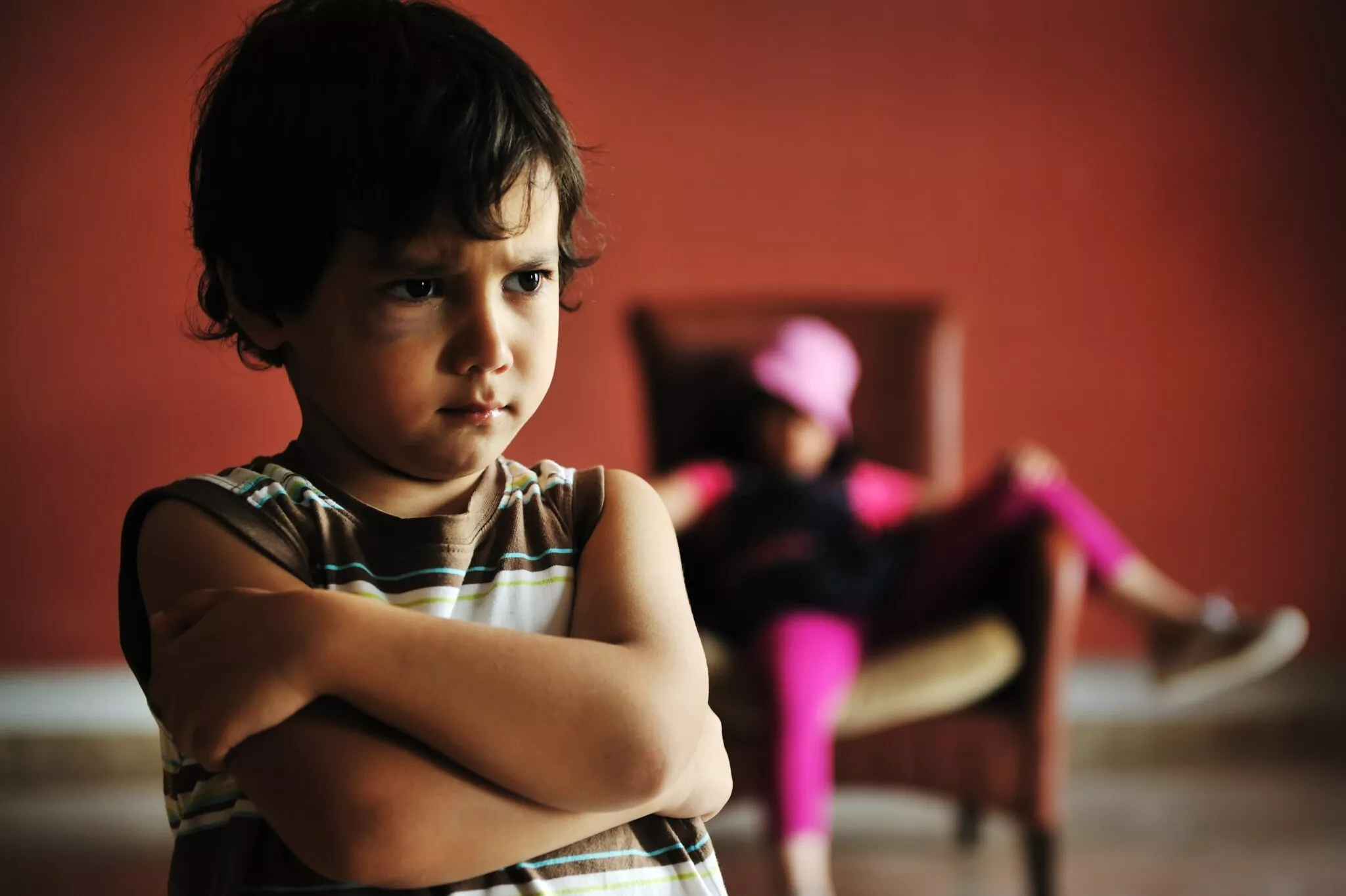 A young boy looking upset with crossed arms in the foreground, a girl sitting in the background on a chair, symbolizing family conflict relevant to Nussbaum family lawyers in Toronto.