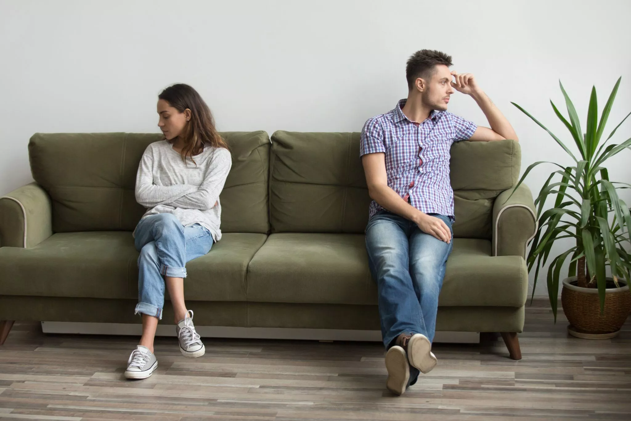 A couple sitting apart on a green sofa looking away from each other, representing relationship conflict often handled by Nussbaum family lawyers in Toronto.