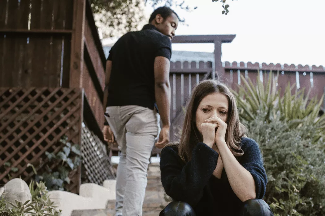 A distressed woman sitting outdoors with a troubled expression and a man walking away in the background, symbolizing family conflict relevant to Nussbaum family lawyers in Toronto.