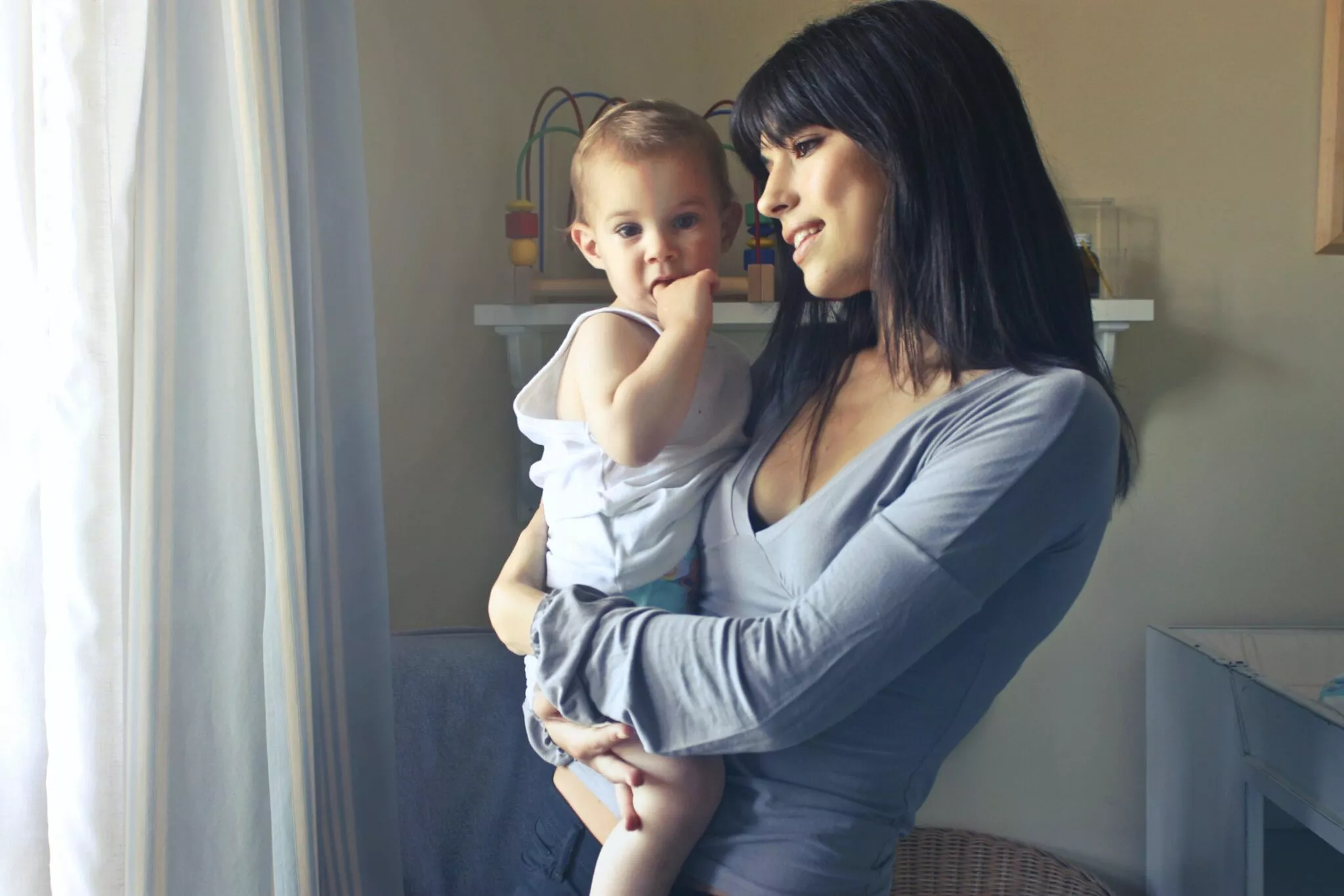 A young mother holding her baby in a softly lit room, symbolizing family care and support, representing the compassionate services of Nussbaum Family Lawyers in Toronto.