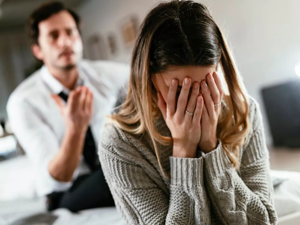 Distressed woman covering her face with her hands while a man in the background gestures in frustration, symbolizing family conflict relevant to Nussbaum Family Lawyers in Toronto