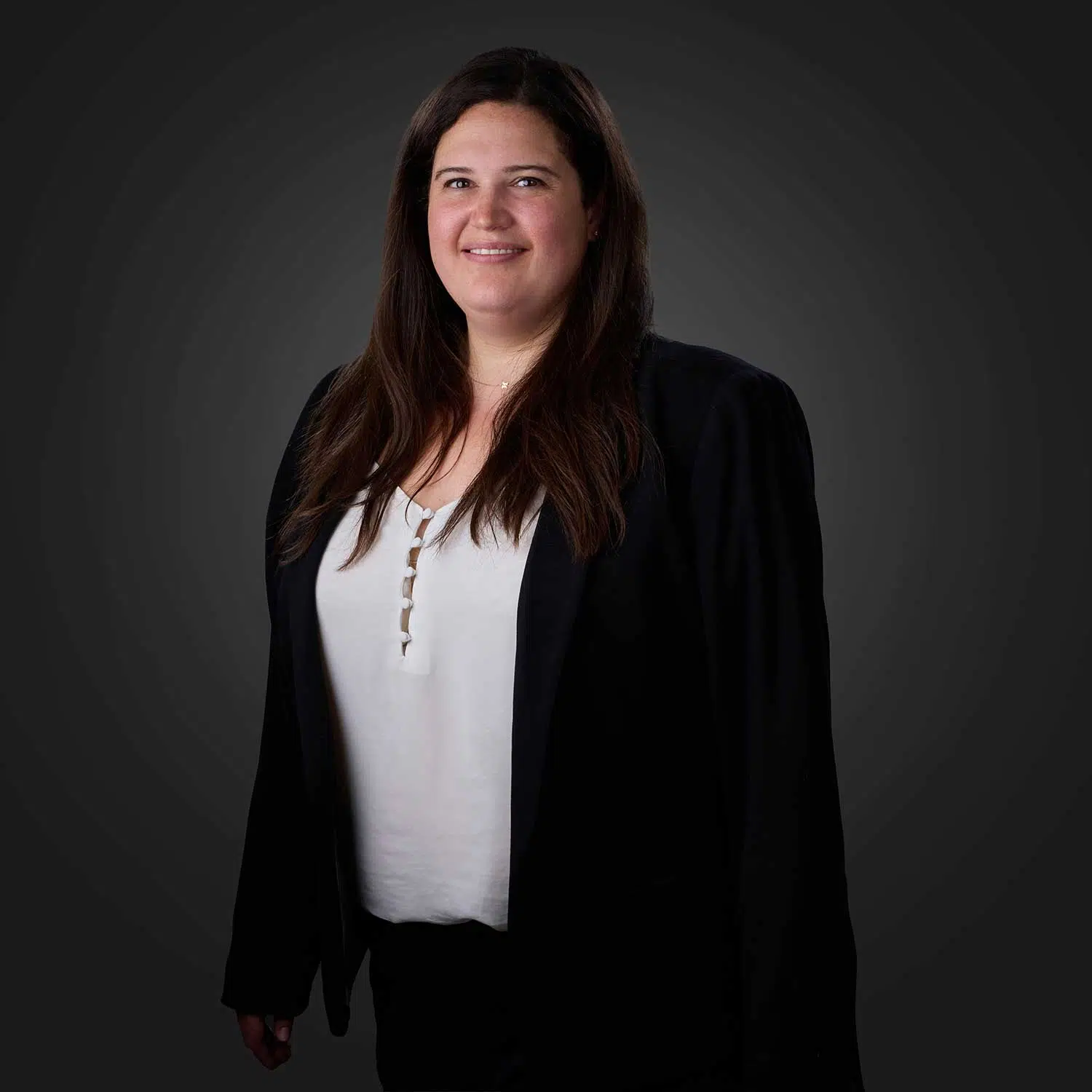 Woman with long dark brown hair wearing a white top and black blazer, smiling against a dark gray gradient background.
