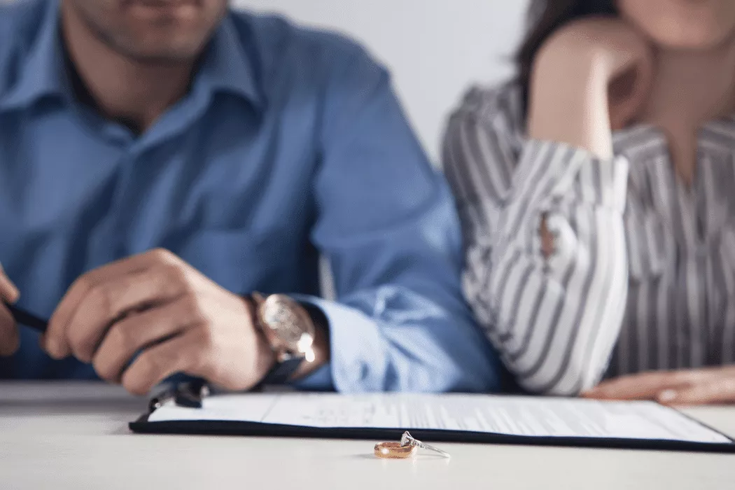 A couple sitting at a table with a legal document and wedding rings in front of them, symbolizing family law issues handled by Nussbaum Family Lawyers in Toronto.