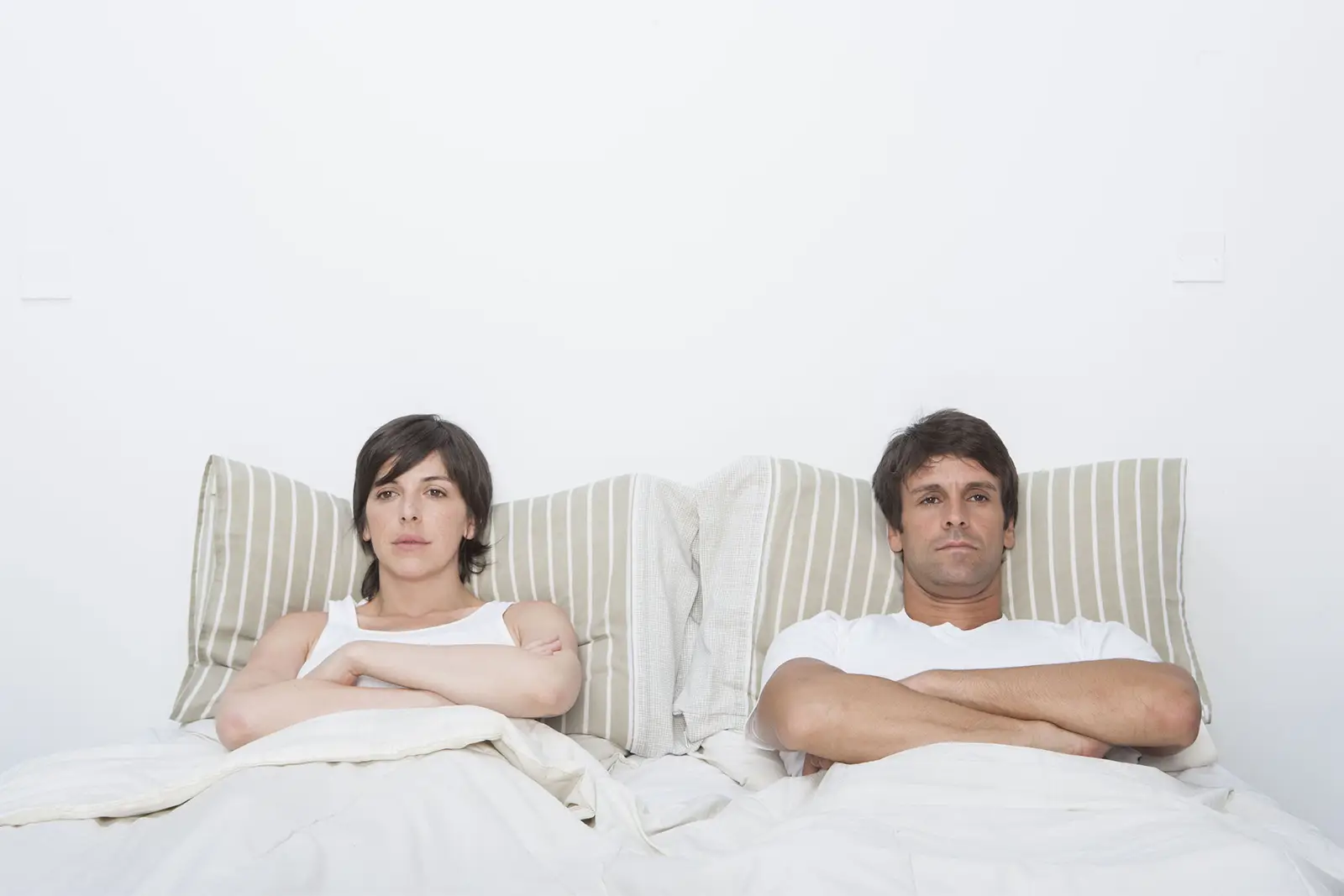 A man and woman sitting in bed back-to-back with arms crossed, reflecting tension and conflict often addressed by Nussbaum family lawyers in Toronto.