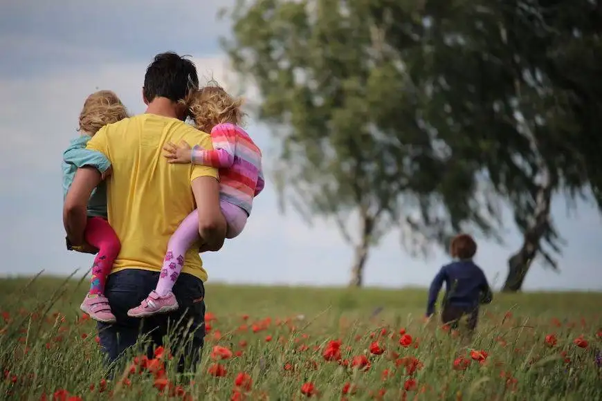 A father walking through a field of red flowers carrying two young children, symbolizing family care and support, reflecting the services of Nussbaum family lawyers in Toronto.