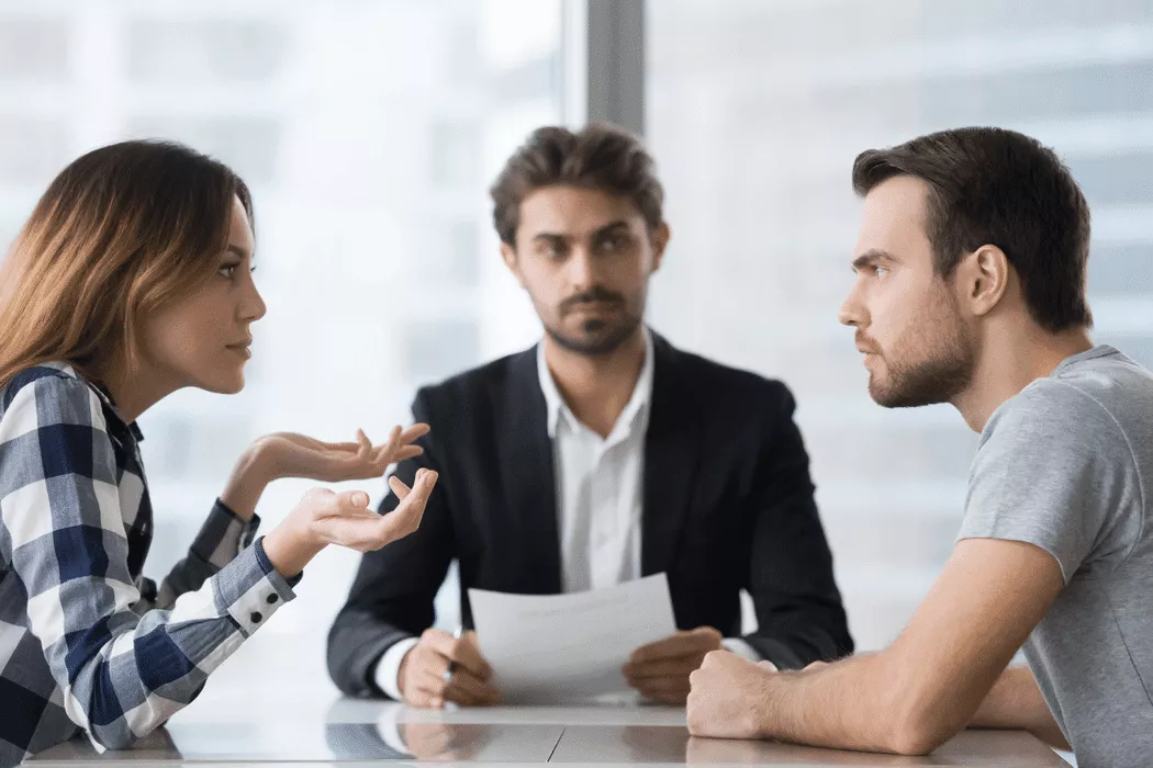 A woman and a man having a serious discussion across a table with a male family lawyer in a suit mediating, symbolizing Nussbaum Family Lawyers in Toronto providing legal support for relationship or custody matters.