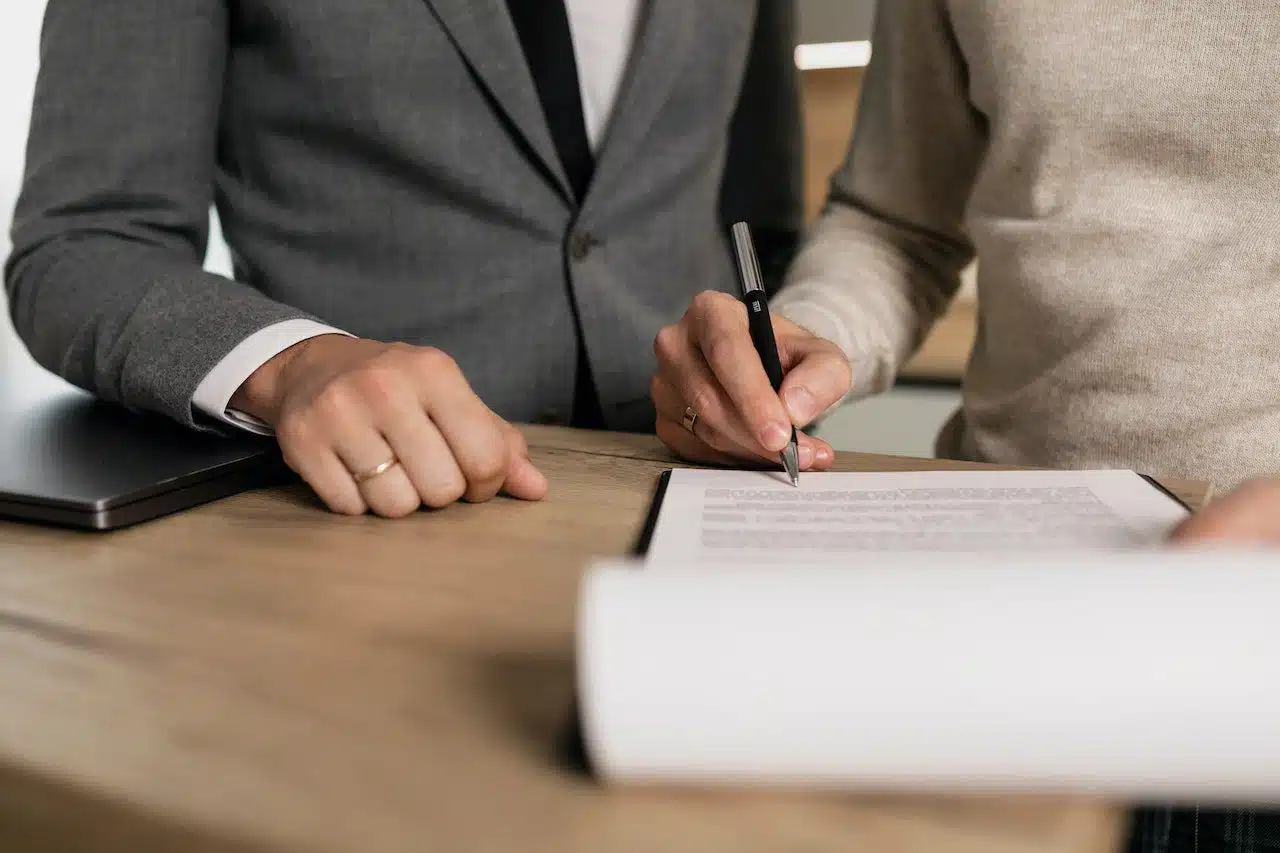 Two individuals seated at a wooden table, one in a grey suit with a wedding ring, the other in a beige sweater, signing a legal document, representing Nussbaum family lawyers in Toronto assisting with family legal matters.
