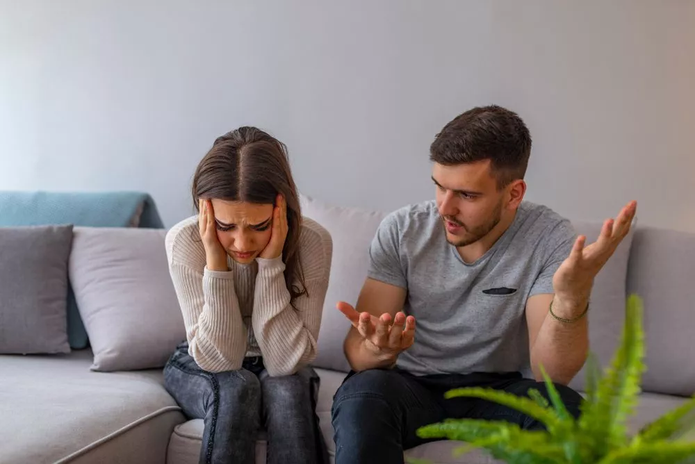 A distressed woman and an upset man sitting on a couch in a home setting, illustrating a tense family dispute situation relevant to Nussbaum family lawyers in Toronto.
