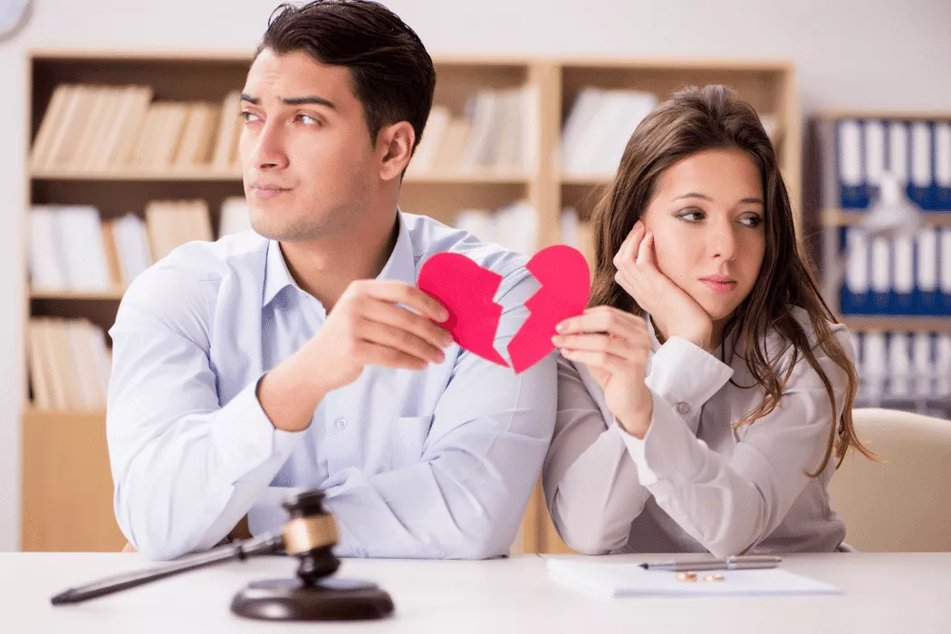 A man and woman sitting apart at a desk holding a torn paper heart, with a gavel and documents nearby, symbolizing a family law dispute in Toronto involving Nussbaum Family Lawyers.