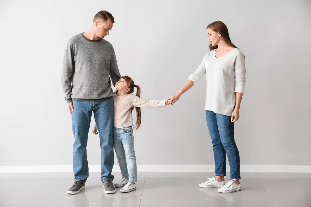 A father, mother, and young daughter standing apart in a neutral space, with the daughter holding both parents' hands, symbolizing family mediation and support relevant to Nussbaum family lawyers in Toronto.