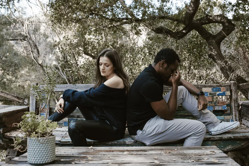 A distressed couple sitting back-to-back on a weathered wooden bench in an outdoor setting, symbolizing conflict and the need for family law support from Nussbaum Family Lawyers in Toronto.