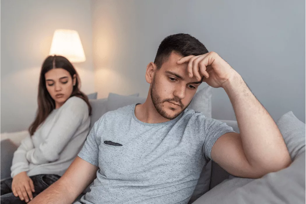 A distressed couple sitting apart on a couch in a softly lit room, symbolizing relationship difficulties addressed by Nussbaum family lawyers in Toronto.